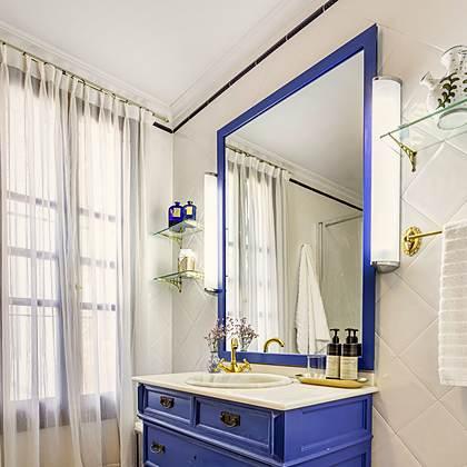 Ba&ntilde;o de Villa Paula con c&oacute;moda antigua pintada de azul reconvertida en tocador, espejo a juego y grifer&iacute;a dorada
