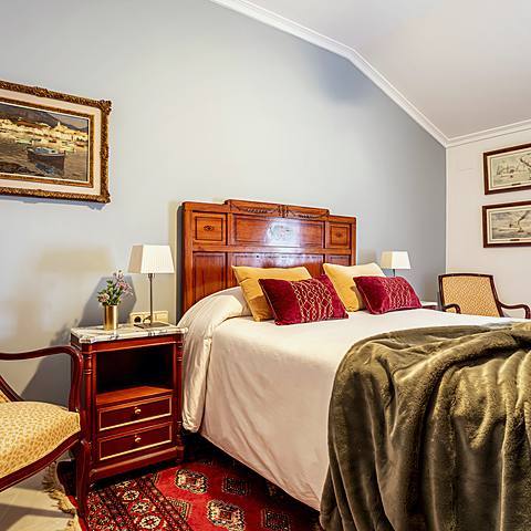 Habitaci&oacute;n Naval de Villa Paula, con cabecero tallado y cuadros de puertos y veleros