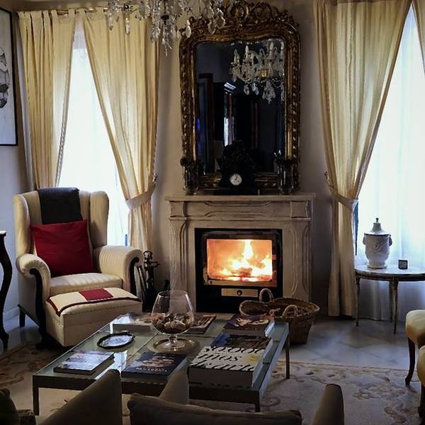Sal&oacute;n de Villa Paula con chimenea encendida y espejo dorado