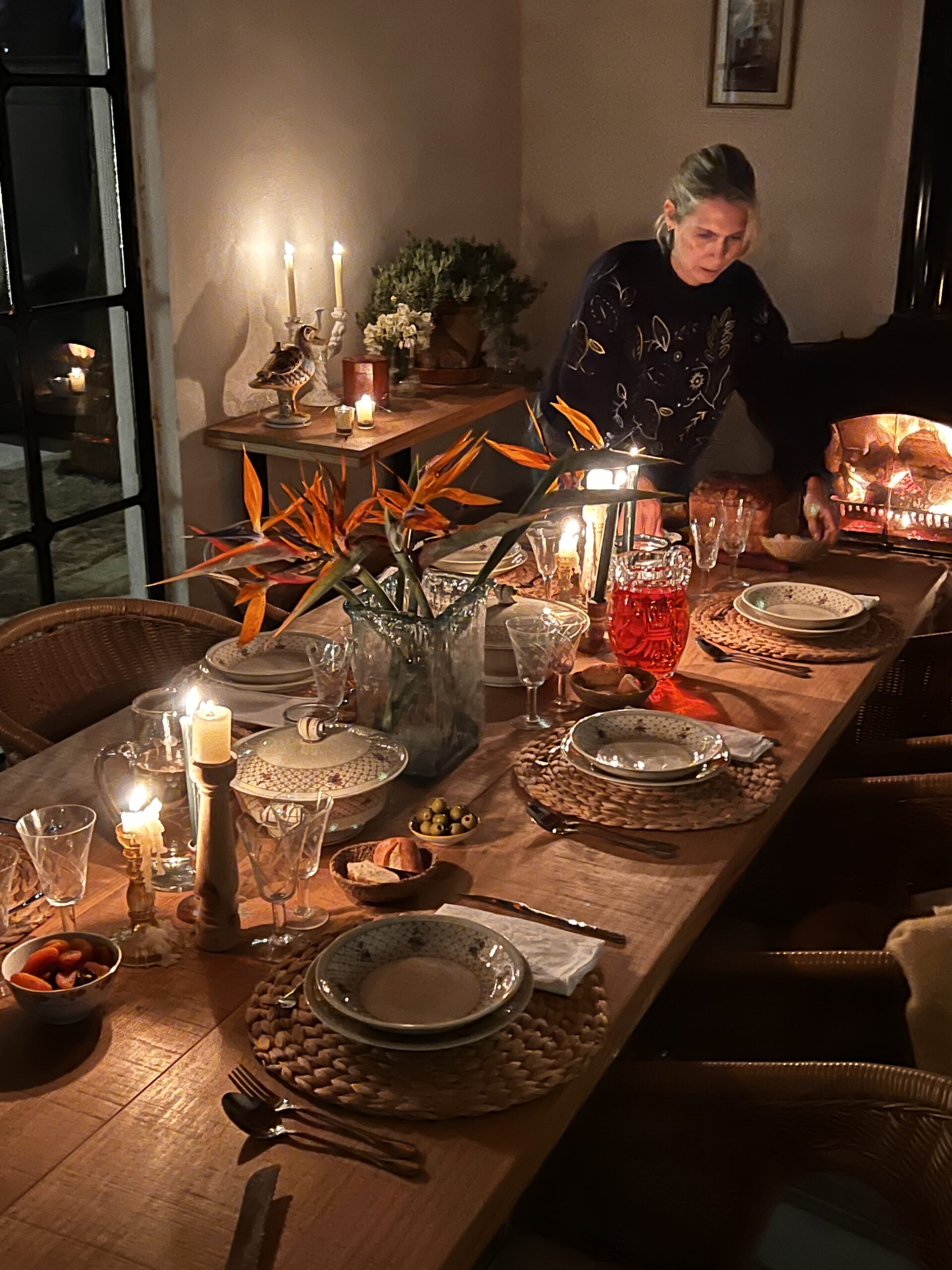 Mesa larga del cenador de noche, con la chimenea encendida, en Villa Paula