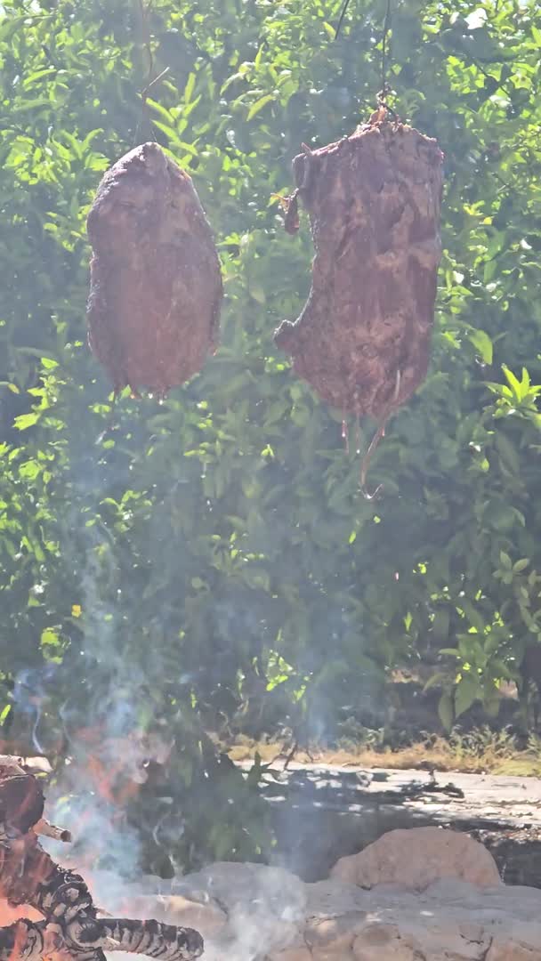 Carne colgada sobre la brasa, entre el humo, en el jardín de Villa Paula